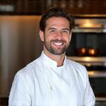 Portrait souriant d'Aurélien Dubois, Chef Exécutif, dans une cuisine étoilée.